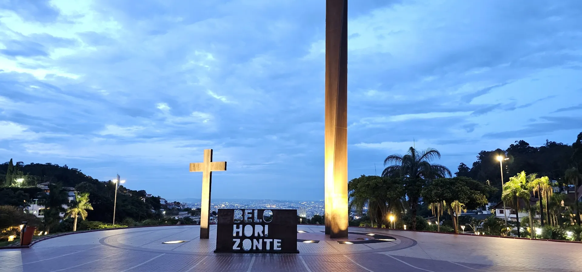 Mirante da Praça do Papa em Belo Horizonte, com a cruz, o letreiro da cidade e o monumento iluminados ao entardecer