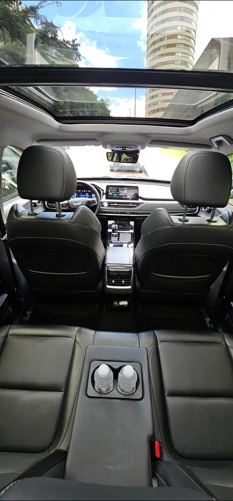 Interior do SUV executivo com bancos de couro, teto solar panorâmico e água no porta-copos, em transfer do Belvedere para o Aeroporto de Confins