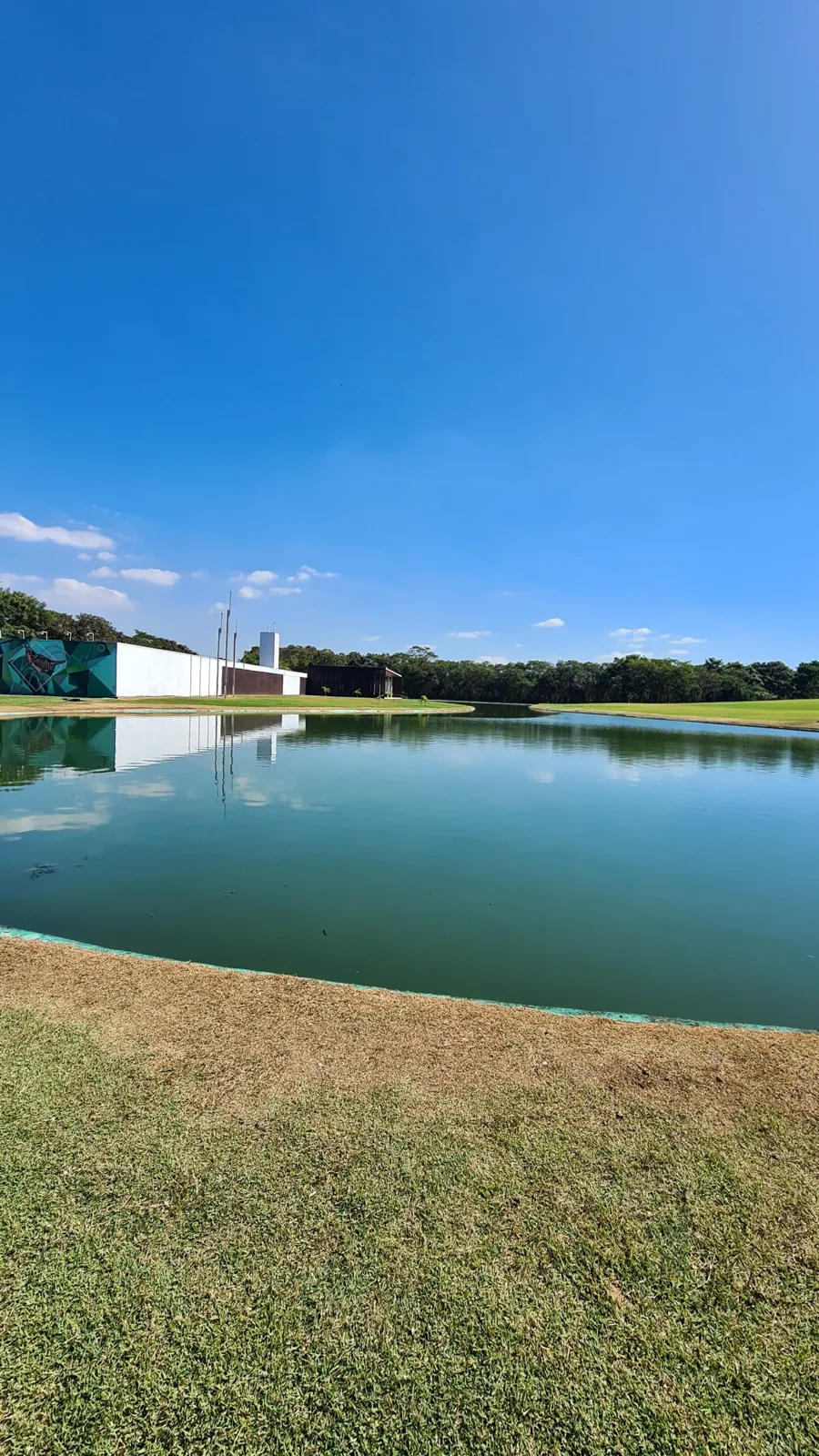 Lago e gramado do Parque Ecológico da Pampulha, com painel verde e céu azul, em Belo Horizonte